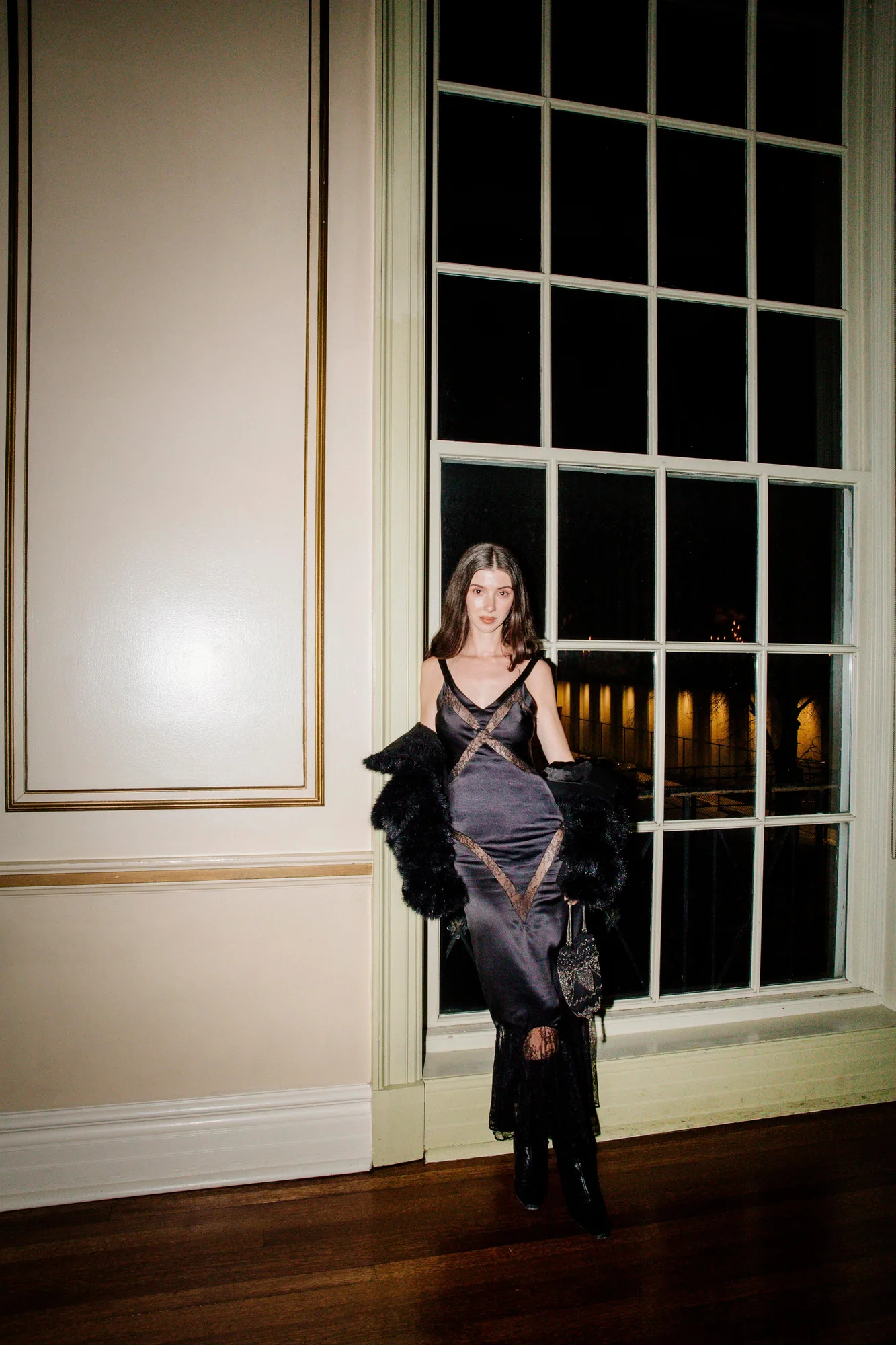 Woman in a draped black gown standing in a panelled doorway