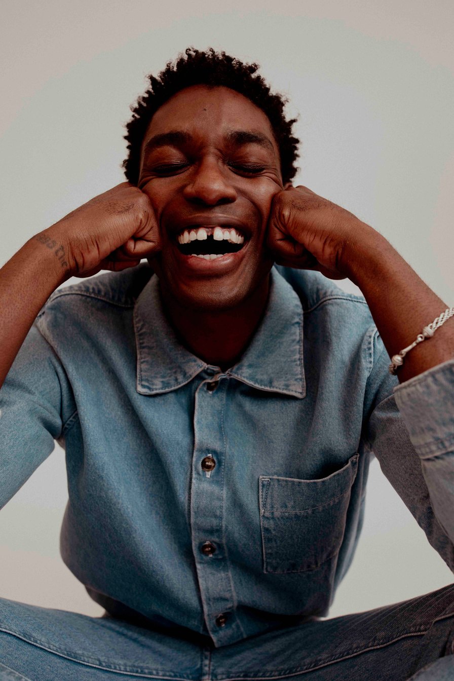 Portrait of a smiling man in a denim shirt holding his cheeks