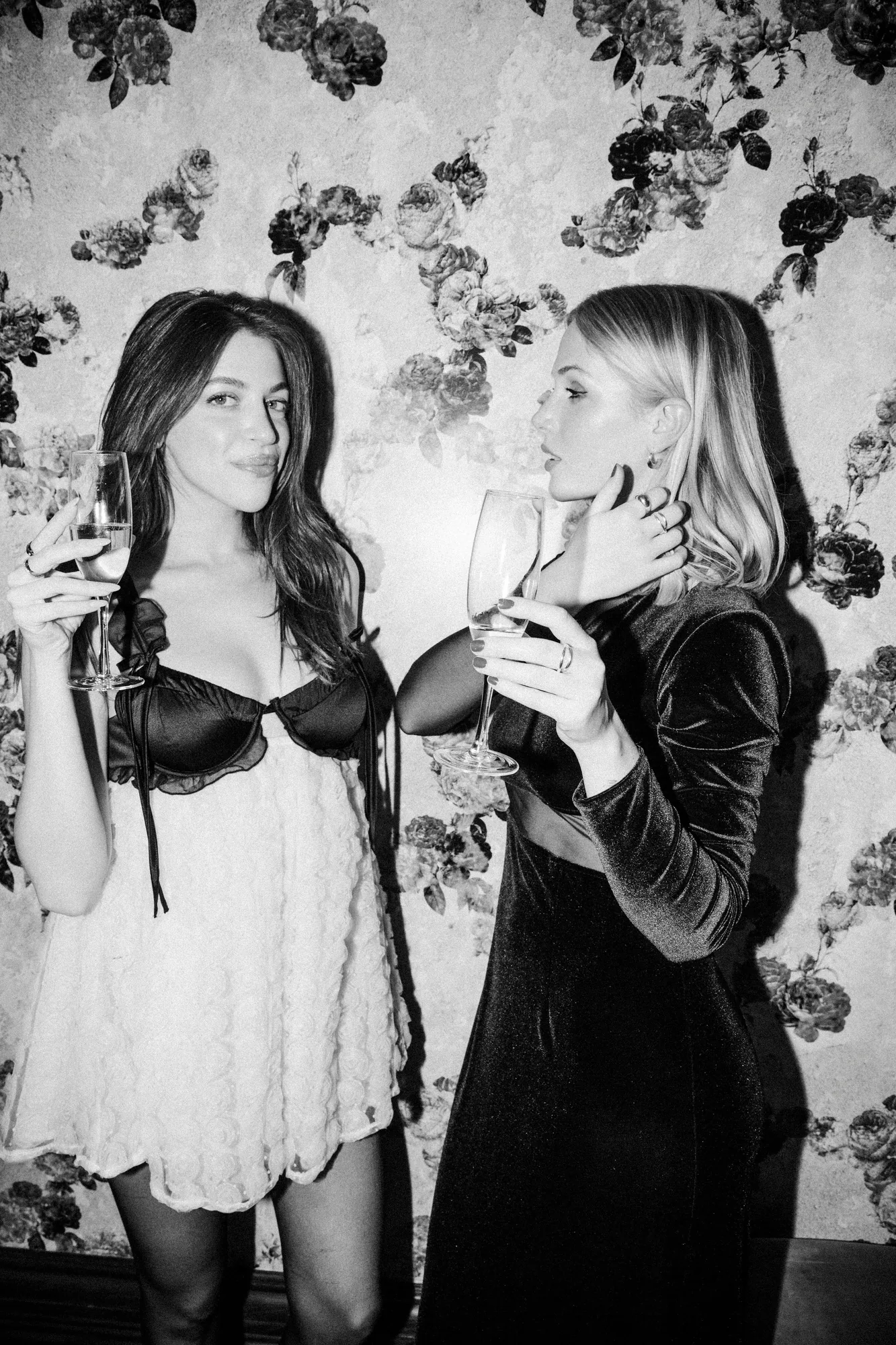 Black and white shot of two women with champagne coupes against floral wallpaper