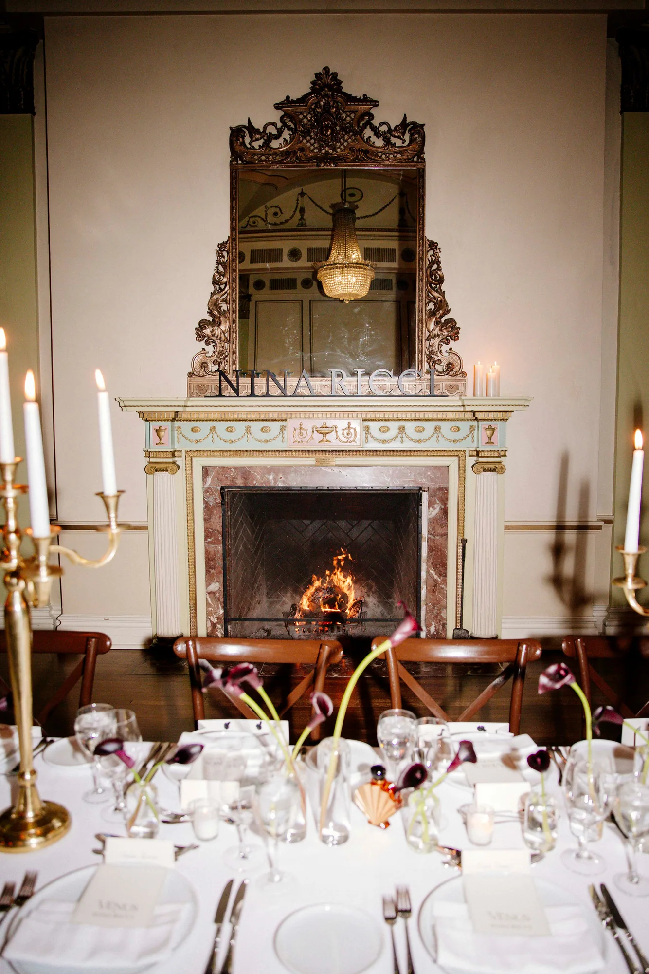 Banquet table set before a gilded fireplace with candelabra