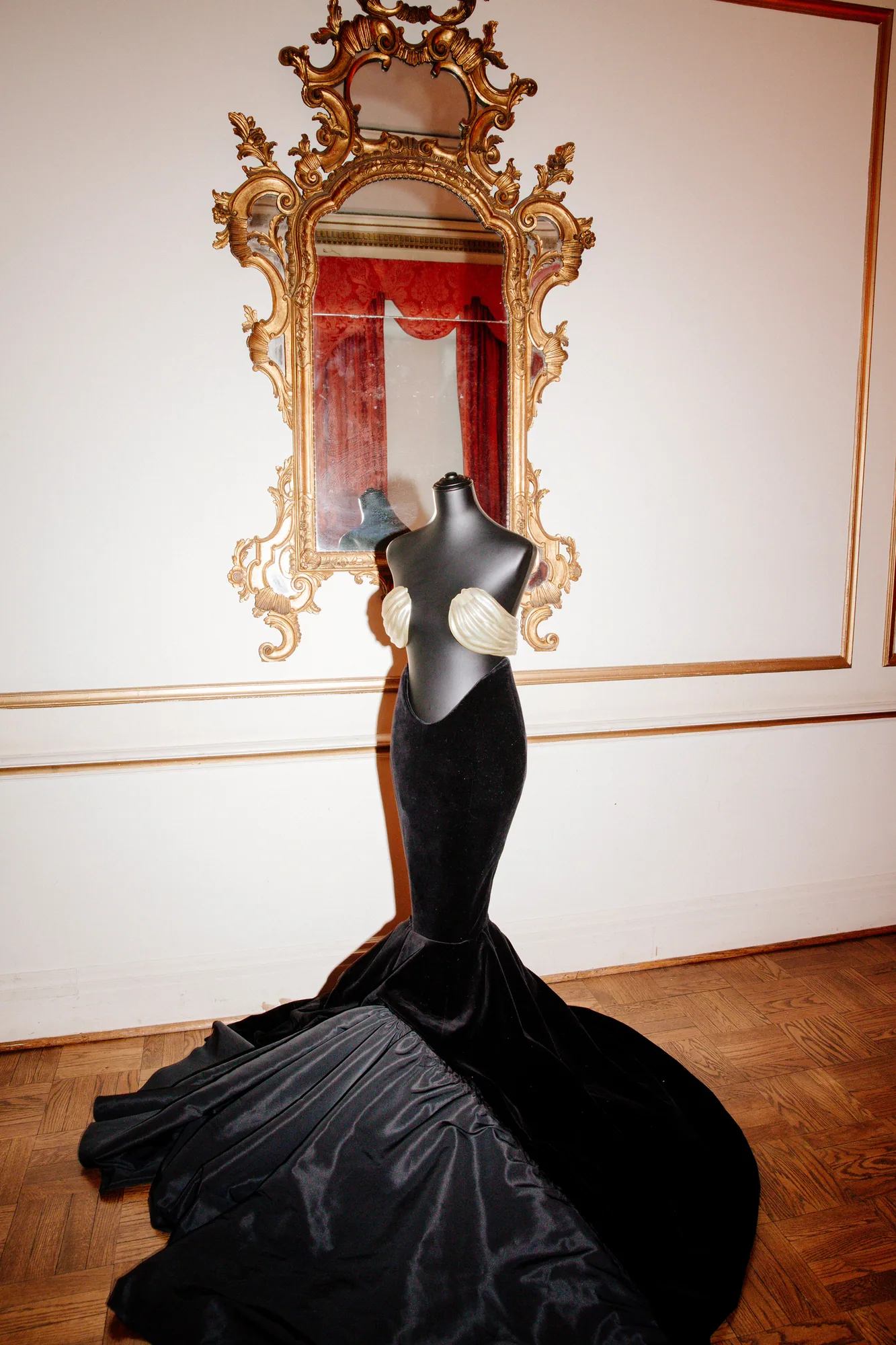 Woman in a voluminous black gown standing before a gilded mirror