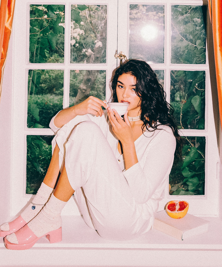 Woman in white seated in a window with a drink