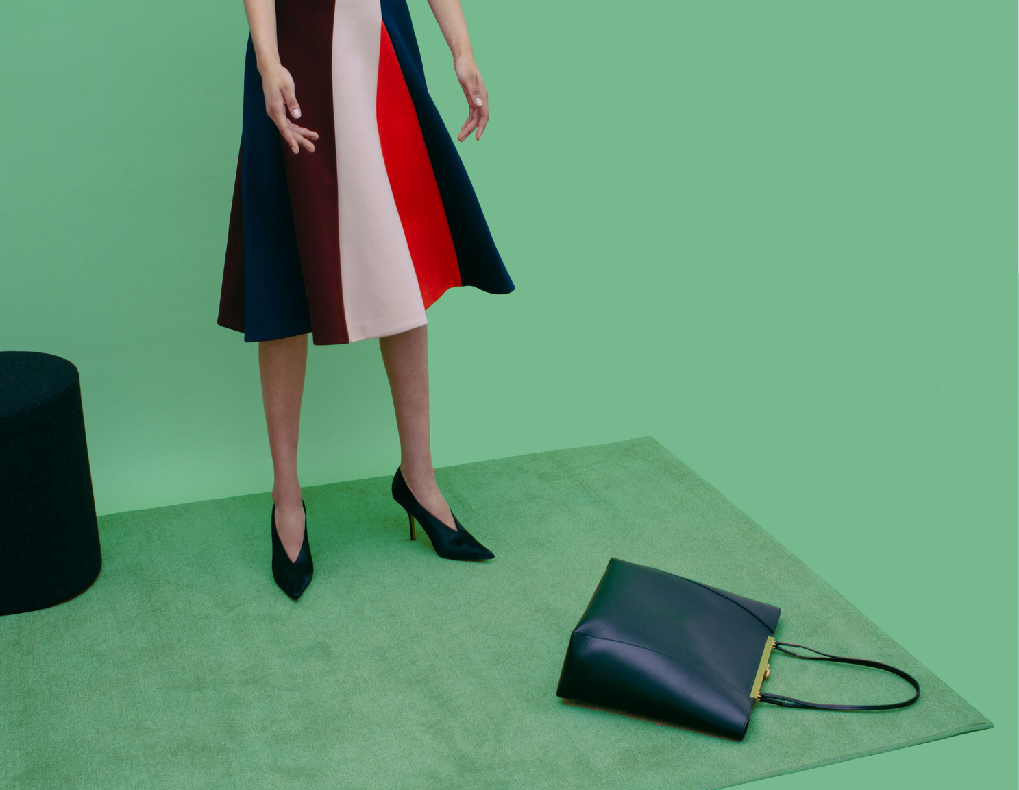 Colour-block skirt and black handbag against a green set