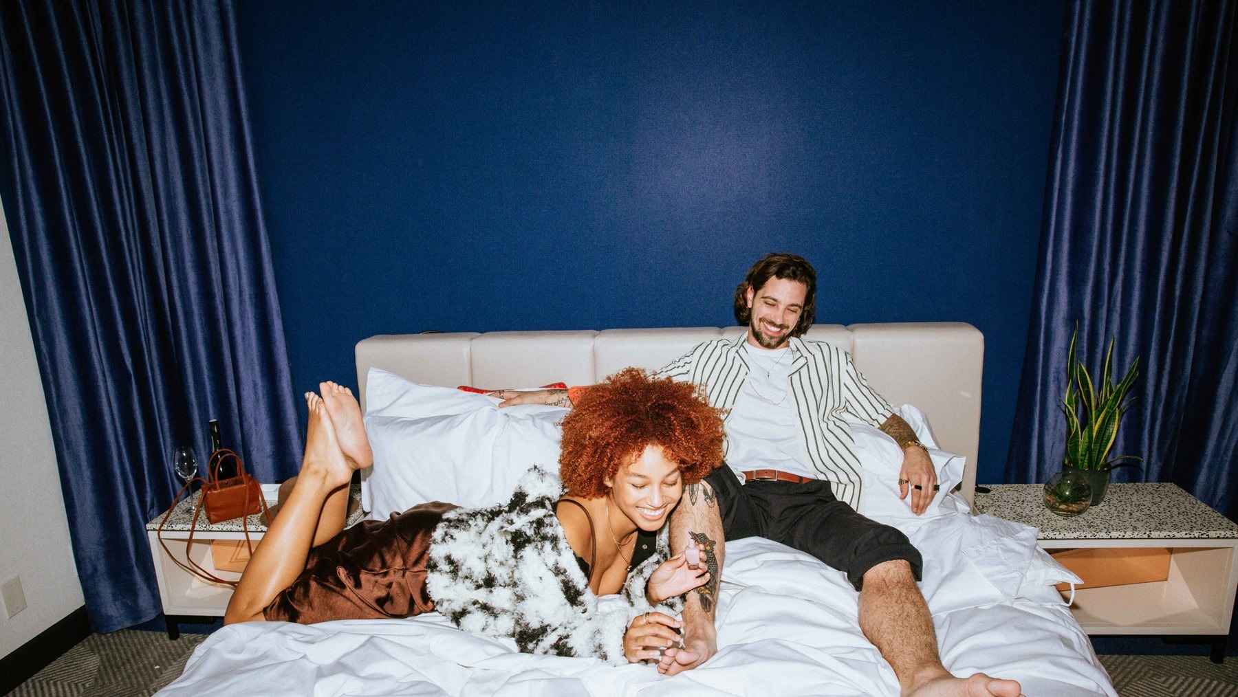Couple laughing on a hotel bed against a deep blue wall
