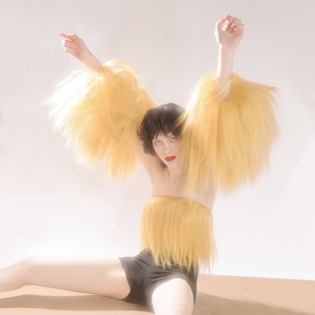 Model in a yellow feathered top with arms outstretched