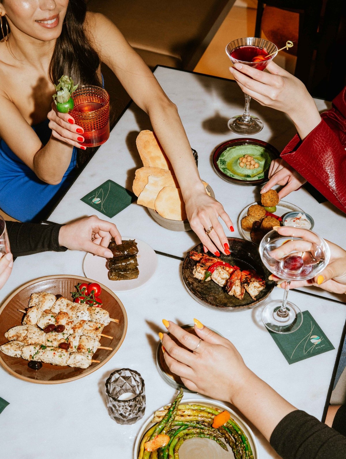 Overhead shot of hands sharing dishes and cocktails at a dinner table