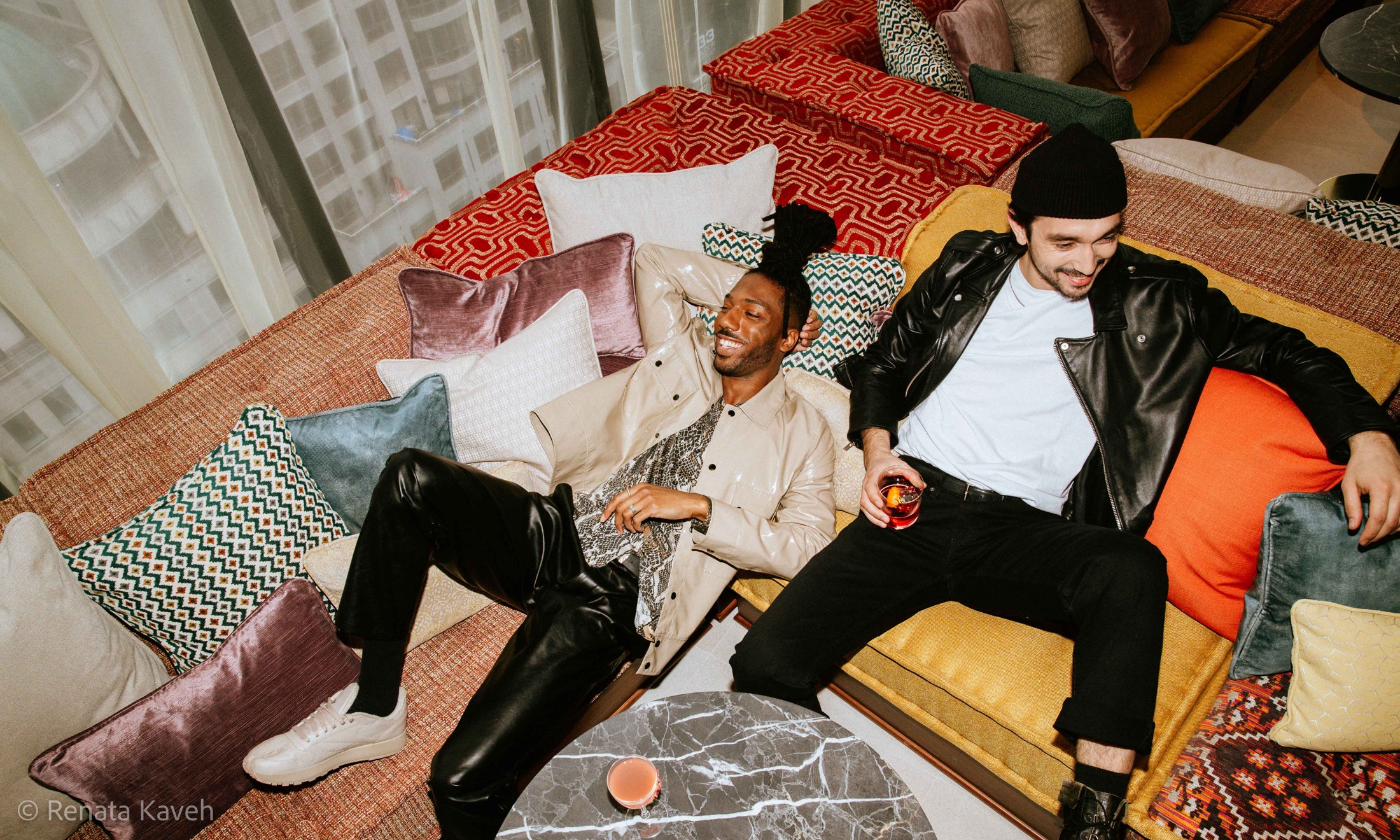 Two men lounging among colourful cushions with drinks