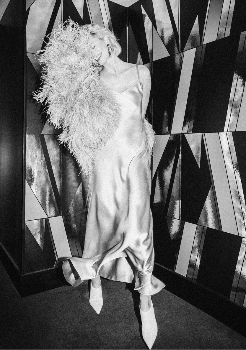 Black and white portrait in a feathered outfit against a geometric backdrop