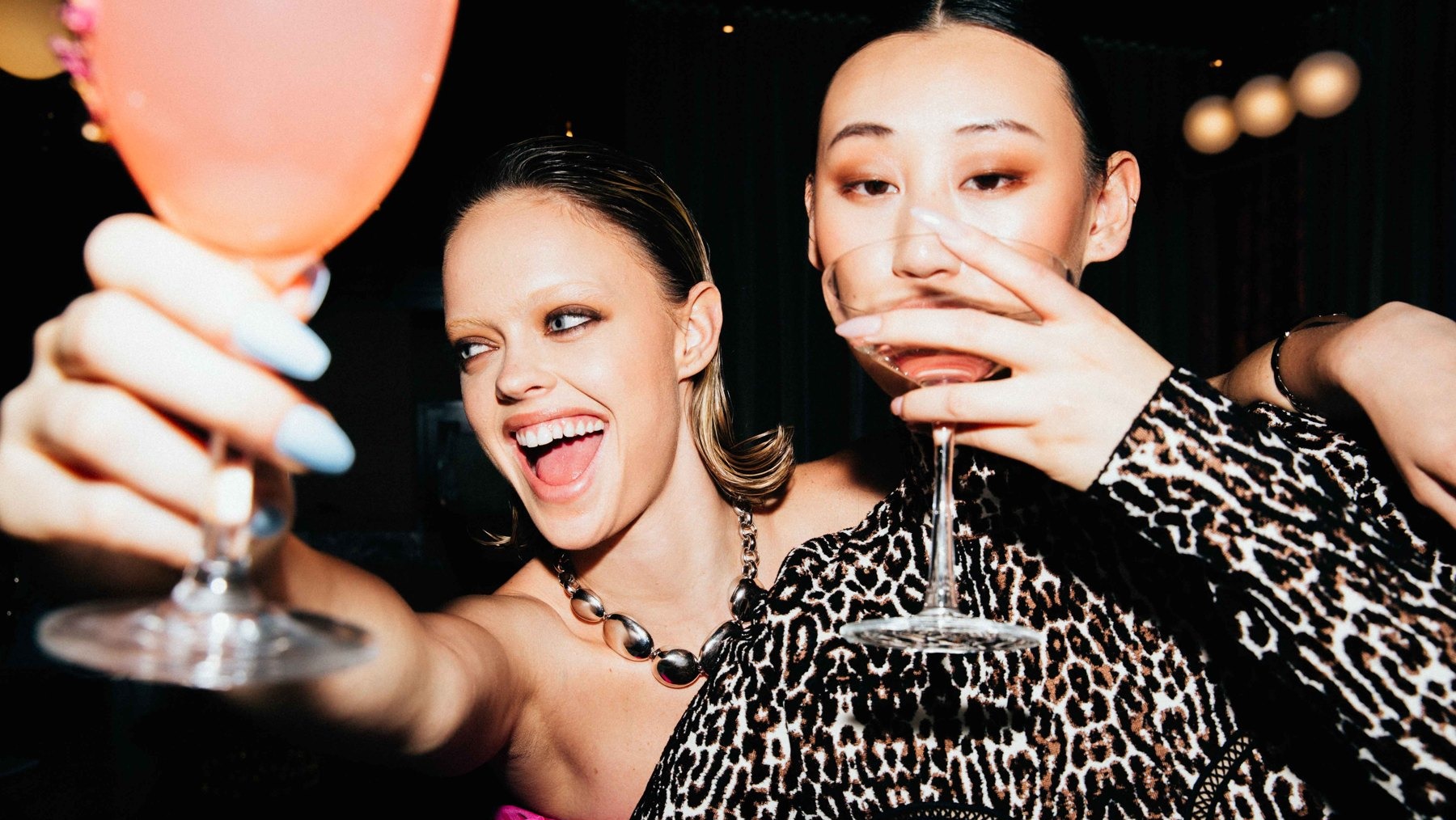 Two women toasting with cocktails at a party
