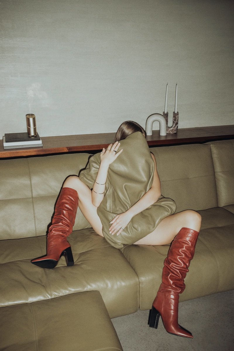 Person on a sofa holding an olive pillow, wearing red leather boots
